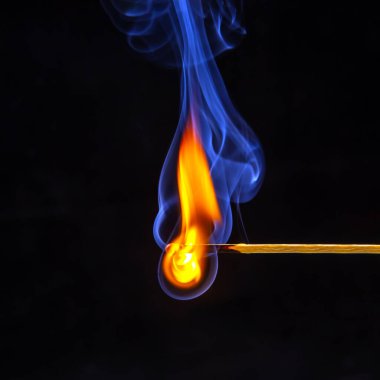 Karanlık bir arka planda yanıp tutuşan ahşap kibrit. Yanan bir ağaçtan gelen parlak ateş ve duman.