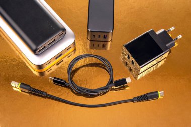 Güç bankası ve elektrik prizi, altın bir arka planda kablolu yayın. Cihazları şarj etmek için elektronik aygıtlar