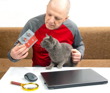 Adam internetten almak için dizüstü bilgisayarın arka planında bir ev modeline bakıyor. Kendi evine sahip olmanın hayalini kur. Konut satın alma kavramı.