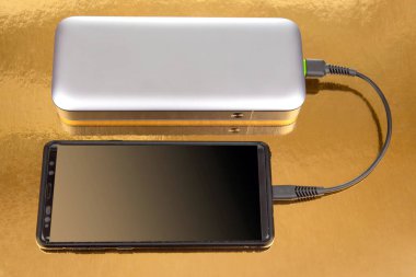 Powerbank altın arka planda bir akıllı telefondan para alıyor. Cihazları ve akıllı telefonları şarj etmek için elektronik aygıtlar