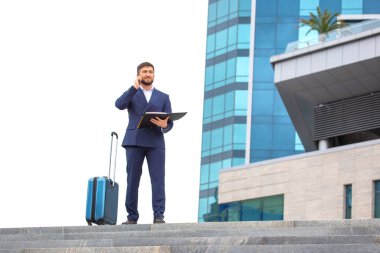 Başarılı bir iş adamı, elinde belgelerle bir ofis binasının arka planındaki basamaklarda duruyor.