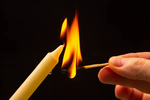 Lighting a candle with a wooden match on a dark background. Burning candle fire