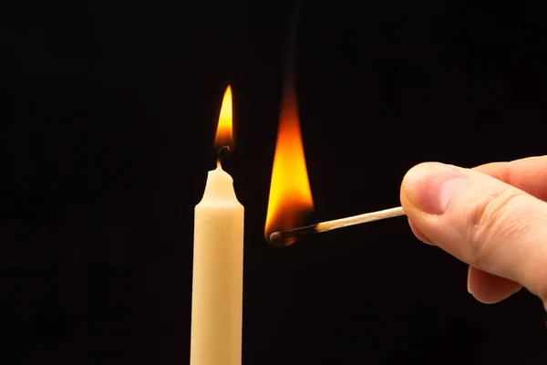 stock image Lighting a candle with a wooden match on a dark background. Burning candle fire