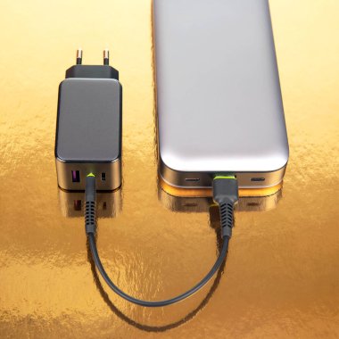 Güç bankası ve elektrik prizi, altın bir arka planda kablolu yayın. Cihazları şarj etmek için elektronik aygıtlar