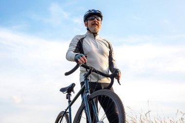 Sakallı adam bisikletçi mavi gökyüzüne karşı bir bisikletle duruyor. bisiklet ve sağlık hobileri