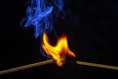 Ateş ve duman. Siyah arka planda yanan ve tüten kibrit. Sıcaklık ve alevlerin ışığı