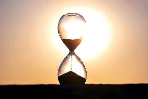 Hourglassは 夜の太陽の背景に対して時間の長さを数えています 宇宙における生命時間の流動性という概念 時間と光 — ストック写真