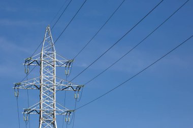 Mavi gökyüzünün arka planında voltaj iletim kabloları olan elektrik kulesi. Yüksek voltaj kulesi. Elektrik iletimi için kablolarla elektrik hattı desteği. Enerji endüstrisi.