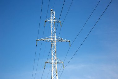 Mavi gökyüzünün arka planında voltaj iletim kabloları olan elektrik kulesi. Yüksek voltaj kulesi. Elektrik iletimi için kablolarla elektrik hattı desteği. Enerji endüstrisi.