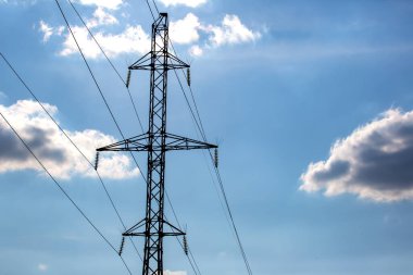 Mavi gökyüzünün arka planında voltaj iletim kabloları olan elektrik kulesi. Yüksek voltaj kulesi. Elektrik iletimi için kablolarla elektrik hattı desteği. Enerji endüstrisi.