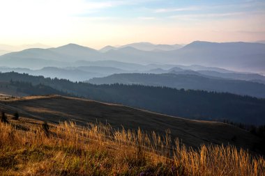 Gün batımında gökyüzünde renkli bulutlar, dağlık bir orman alanının arka planına karşı..