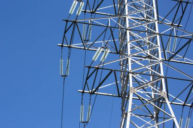 Mavi gökyüzünün arka planında voltaj iletim kabloları olan elektrik kulesi. Yüksek voltaj kulesi. Elektrik iletimi için kablolarla elektrik hattı desteği. Enerji endüstrisi.