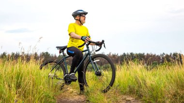 Sarı elbiseli sakallı bisikletçi doğada bir bisikletin üzerinde dinleniyor. Spor, hobiler ve sağlık için eğlence