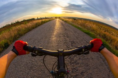Eller direksiyonda, gün batımına doğru bisiklet sürüyor. Bakış açısı
