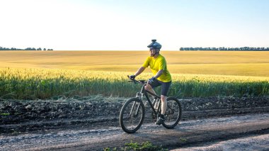 Sarı elbiseli bir bisikletçi doğada bir yolda bisiklet sürüyor. Spor, hobiler ve sağlık için eğlence