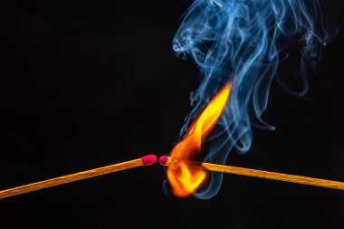 Ateş ve duman. Siyah arka planda yanan ve tüten kibrit. Sıcaklık ve alevlerin ışığı