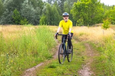 Sarı elbiseli sakallı bir bisikletçi doğada bir yolda bisiklet sürüyor. Spor, hobiler ve sağlık için eğlence