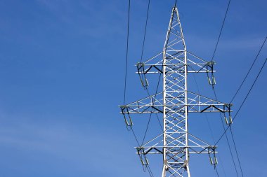 Mavi gökyüzünün arka planında voltaj iletim kabloları olan elektrik kulesi. Yüksek voltaj kulesi. Elektrik iletimi için kablolarla elektrik hattı desteği. Enerji endüstrisi.