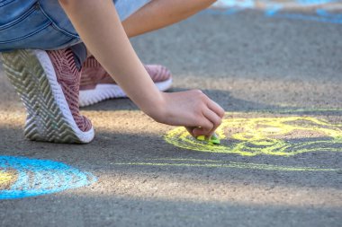 Kız asfalta sarı tebeşirle gülen bir yüz çiziyor. Çocukların eğlence ve eğlencelerinin yaratıcılığı ve hobileri