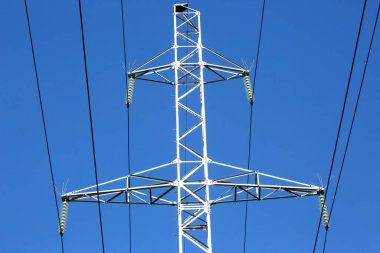 Mavi gökyüzünün arka planında voltaj iletim kabloları olan elektrik kulesi. Yüksek voltaj kulesi. Elektrik iletimi için kablolarla elektrik hattı desteği. Enerji endüstrisi.