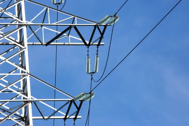 Mavi gökyüzünün arka planında voltaj iletim kabloları olan elektrik kulesi. Yüksek voltaj kulesi. Elektrik iletimi için kablolarla elektrik hattı desteği. Enerji endüstrisi.