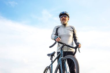 Sakallı adam bisikletçi mavi gökyüzüne karşı bir bisikletle duruyor. bisiklet ve sağlık hobileri