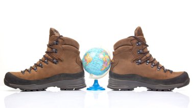 Trekking boots for hiking next to a world globe model on a white background. Equipment for travel and hiking clipart