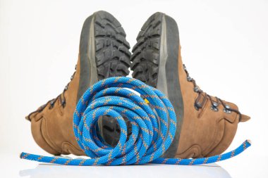 Beyaz arka planda tırmanma ipinin yanında yürüyüş botları. Seyahat ve Yürüyüş Ekipmanı