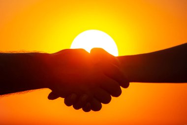 Batan güneşin arka planında erkek ve kadın ellerinin silueti. Toplum ve ailede iletişim ve yakınlık için çabalama kavramı