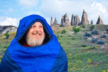 Dağlarda doğanın arka planına karşı uyku tulumunda mutlu sakallı bir adam. Dağlarda doğa yürüyüşleri