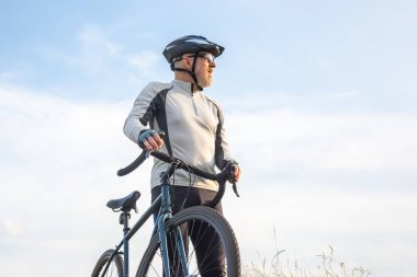 Sakallı adam bisikletçi mavi gökyüzüne karşı bir bisikletle duruyor. bisiklet ve sağlık hobileri