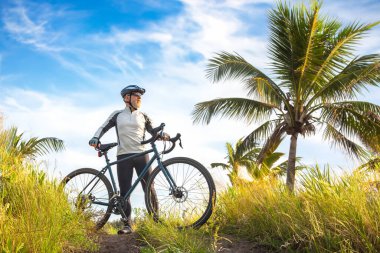 Bisikletli sarı elbiseli sakallı erkek bisikletçi doğadaki palmiye ağaçlarının arka planına karşı. Spor, hobiler ve sağlık için eğlence