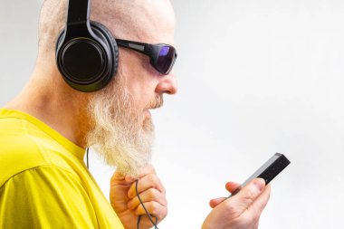 Güneş gözlüklü sakallı adam beyaz arka planda çalan birini kullanarak müzik dinliyor. ses biçimi ve ses teknolojisi