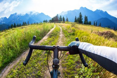 Bir bisikletçinin bisikletinin gidonundaki eller doğada bir patika boyunca gidiyor. Bakış açısı