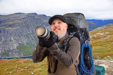 Sırt çantalı sakallı turist fotoğrafçı dağlardaki doğanın güzelliğini fotoğraflıyor. Dağlarda doğa yürüyüşleri