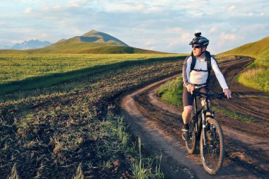 Bisikletçi gün ışığında buğday tarlaları boyunca bisiklet sürüyor.