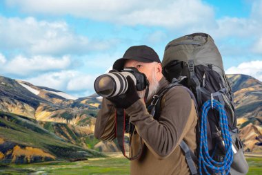 Sırt çantalı sakallı turist fotoğrafçı dağlardaki doğanın güzelliğini fotoğraflıyor. Dağlarda doğa yürüyüşleri