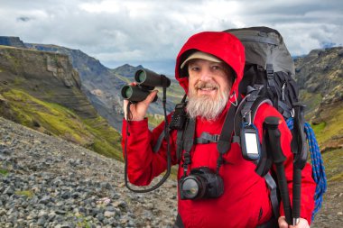 Dağ manzarasında yürüyüş ekipmanları olan mutlu sakallı bir gezgin. Dağlarda doğa yürüyüşleri