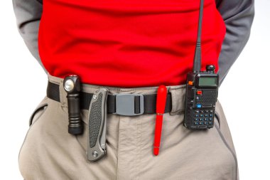 Kalem, telsiz, bıçak ve el feneri, yürüyüş pantolonunun belinde klipslerle. EDC ögeleri