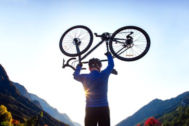 Erkek bisikletçi yükseltilmiş bir bisikletle güneşin ve dağların arka planına karşı