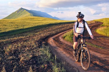 Bisikletçi gün ışığında buğday tarlaları boyunca bisiklet sürüyor.