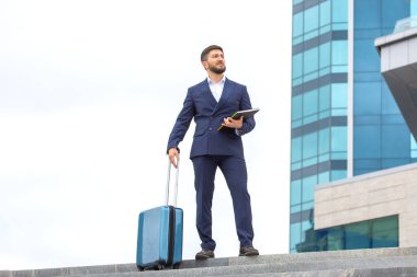 Başarılı bir iş adamı, elinde belgelerle bir ofis binasının arka planındaki basamaklarda duruyor.