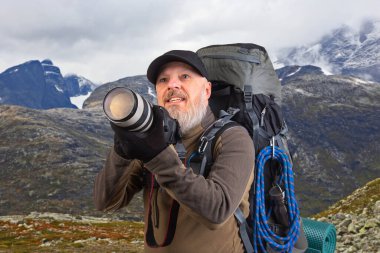 Sırt çantalı sakallı turist fotoğrafçı dağlardaki doğanın güzelliğini fotoğraflıyor. Dağlarda doğa yürüyüşleri