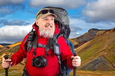 Bir dağ manzarasının arka planına karşı yürüyüş ekipmanlarıyla mutlu sakallı bir gezgin. seyahat, yürüyüş ve macera