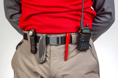 Kalem, telsiz, bıçak ve el feneri, yürüyüş pantolonunun belinde klipslerle. EDC ögeleri