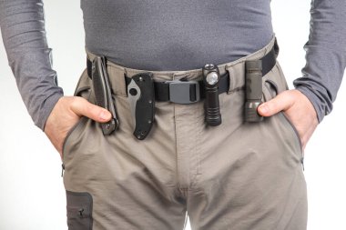 Katlanan bıçak ve turist yürüyüş pantolonunun kemerinde klipsleri olan bir el feneri. EDC ögeleri
