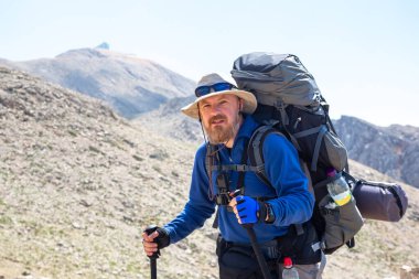 Dağın zirvesine giden yolda büyük bir sırt çantası olan sakallı bir turist.