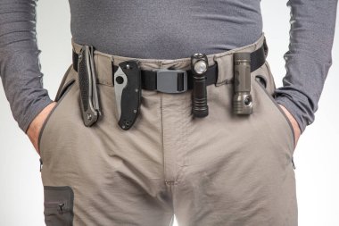 Katlanan bıçak ve turist yürüyüş pantolonunun kemerinde klipsleri olan bir el feneri. EDC ögeleri