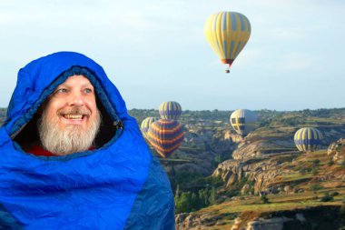 Dağlarda doğanın arka planına karşı uyku tulumunda mutlu sakallı bir adam. Dağlarda doğa yürüyüşleri