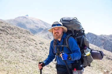 Dağın zirvesine giden yolda büyük bir sırt çantası olan sakallı bir turist.